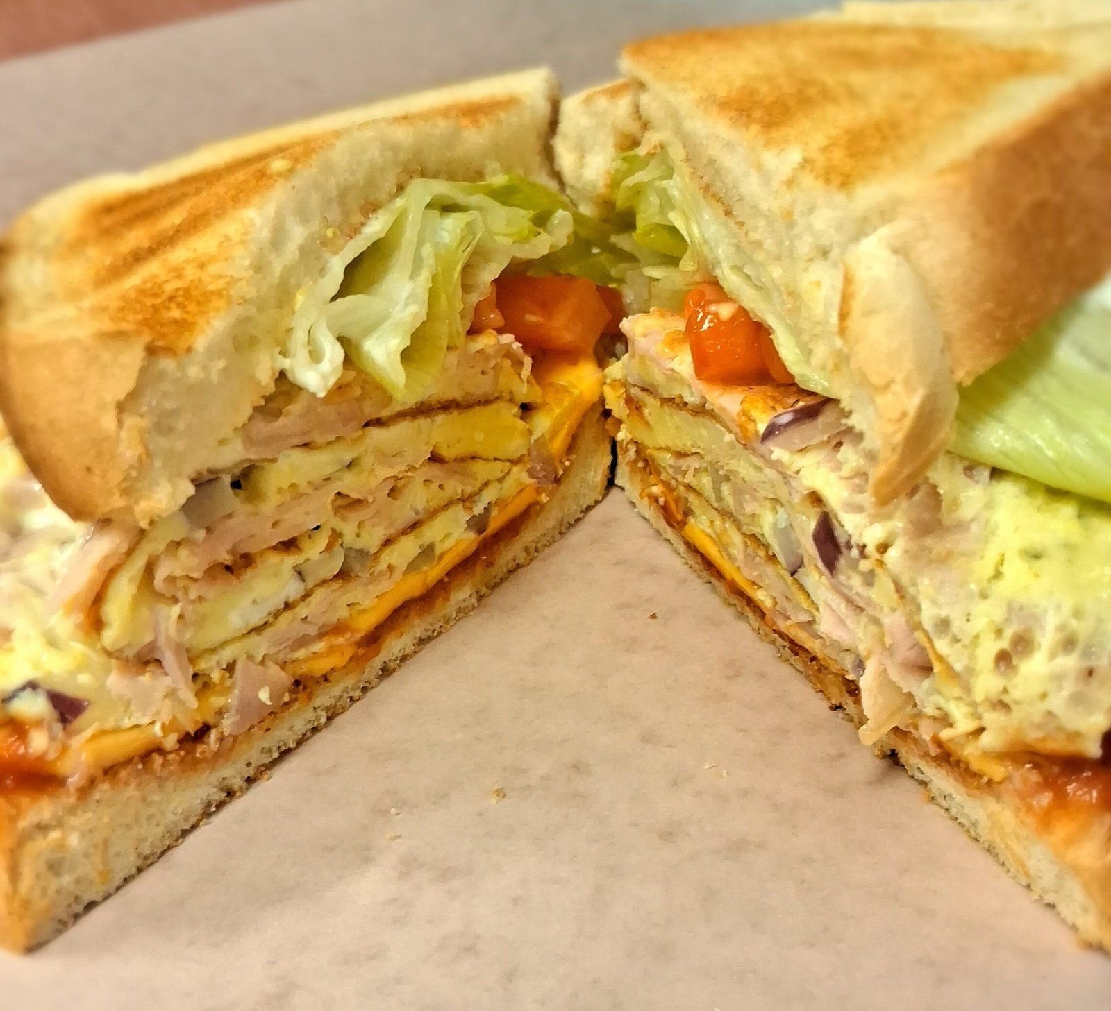 A toasted egg, ham and cheddar sandwich cut in half on deli paper